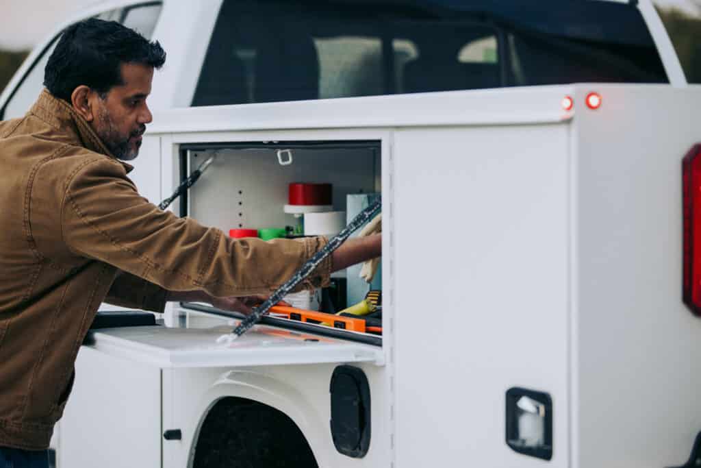 Male Worker Grabbing Cargo from Knapheide Service Truck Compartment
