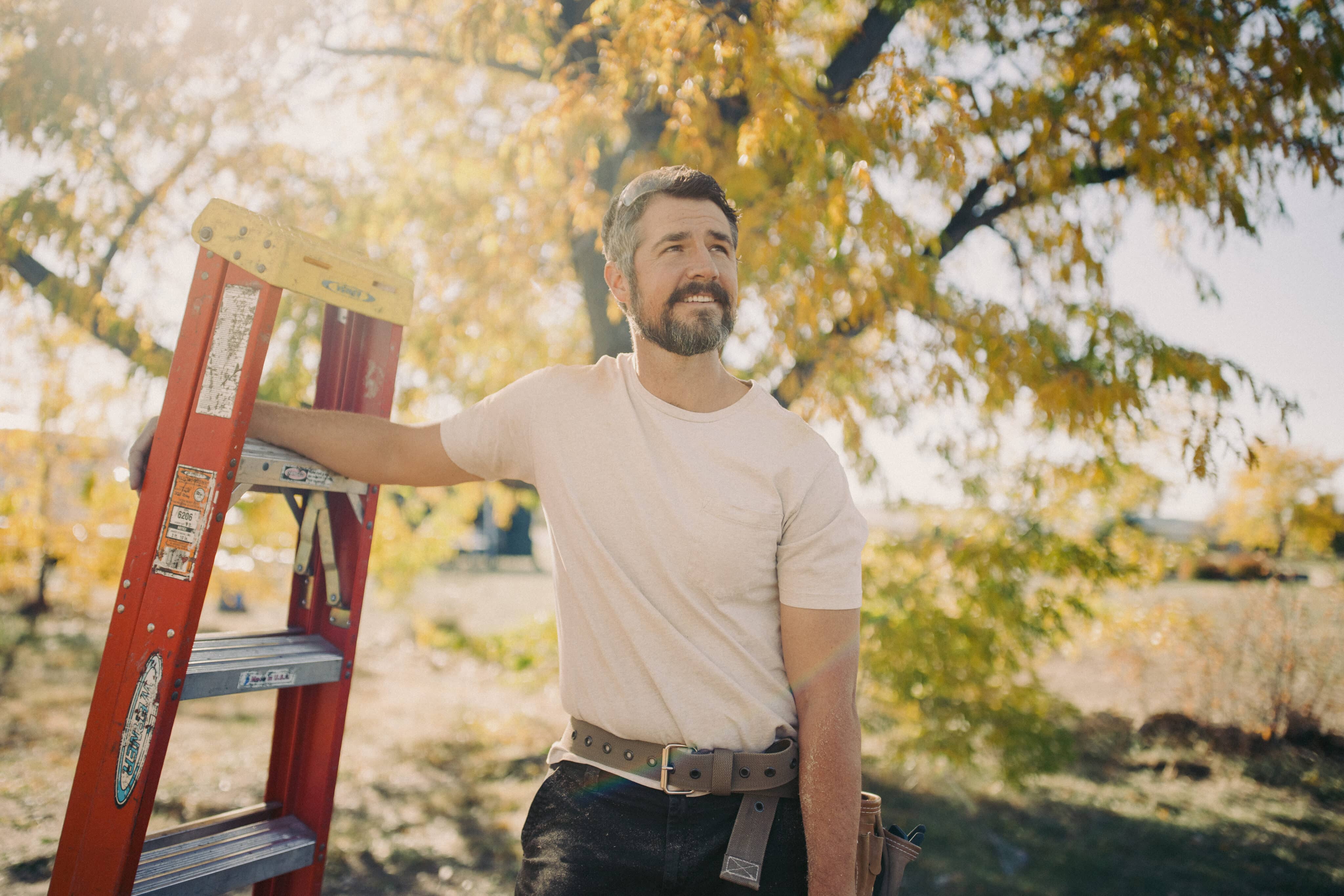 Male Worker Smiling on Jobsite Whiling Holding Ladder